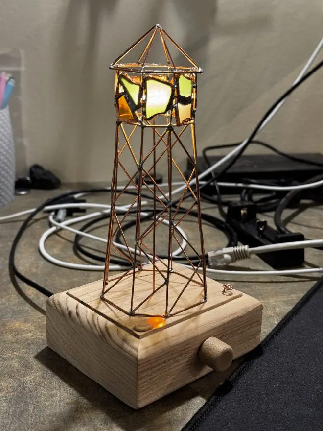 A copper wireframe lighthouse on a wood block with a dial for adjusting brightness